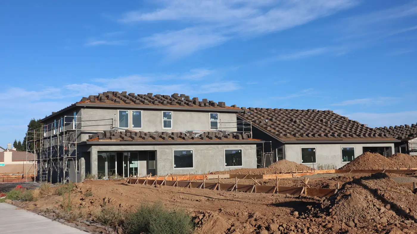 A house under construction with roof tiles on and stucco walls, not yet finished, against a clear sky.