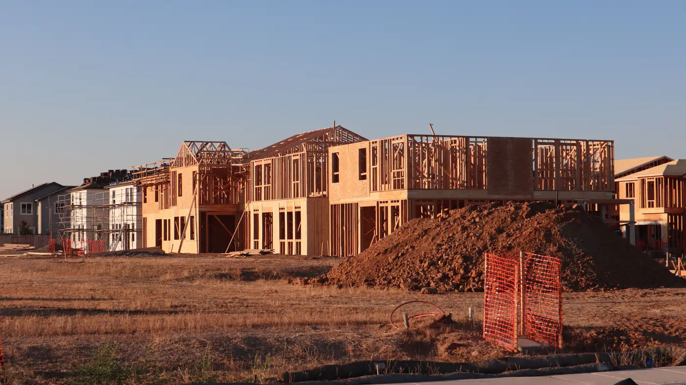 A row of single-family homes at different framing stages along a street in a new subdivision at dusk.